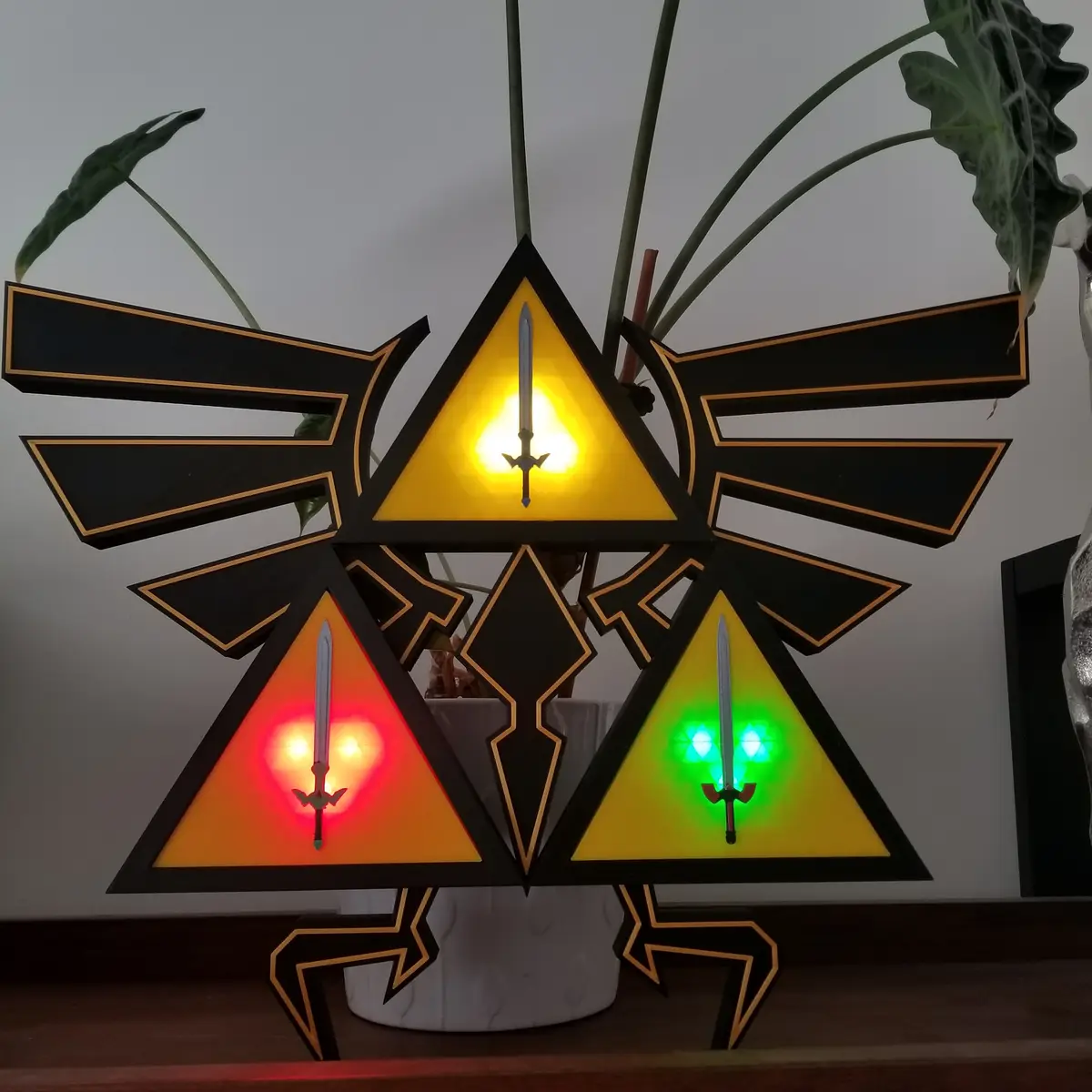 A decorative, illuminated Triforce lamp from The Legend of Zelda, featuring three triangular sections glowing yellow, red…