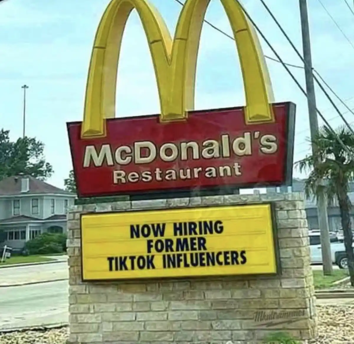 A McDonald's restaurant sign with its iconic golden arches and red background is shown, with a yellow hiring board below it…