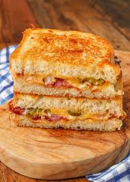 a perfectly grilled cheese sandwich, cut in half and stacked, revealing melted cheese, crispy bacon, and green jalapenos…
