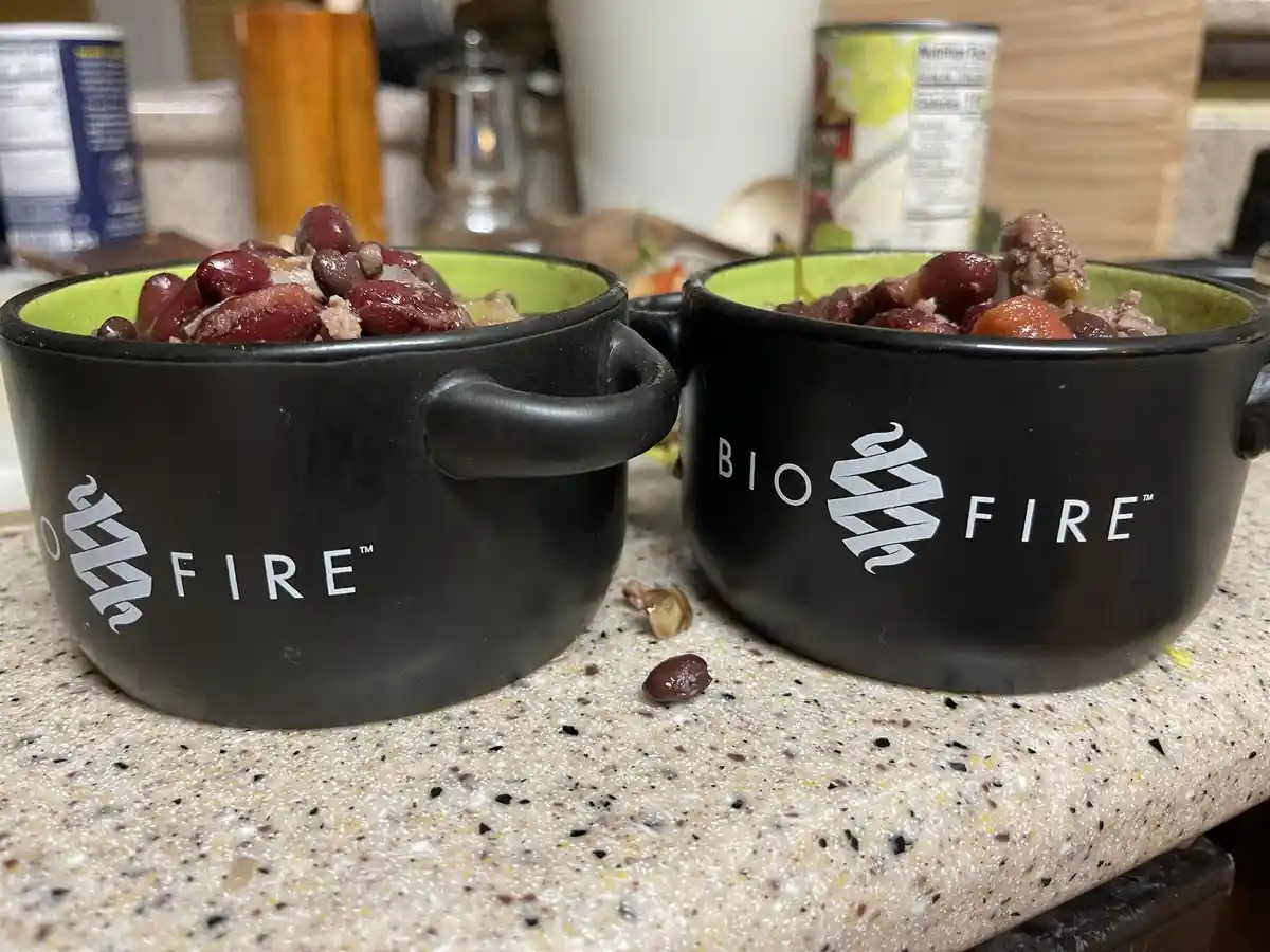 Two black ceramic bowls with handles, branded 'BIOFIRE™' with a stylized flame logo, sit on a speckled countertop filled…