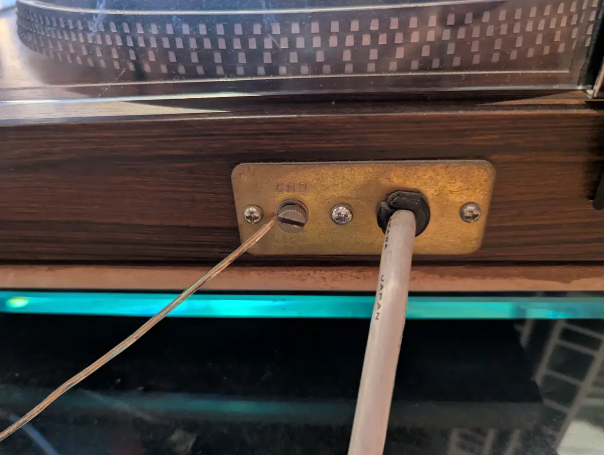 A close-up photo shows a brass grounding plate on a wooden electronic device, with a wire inserted into a screw labeled…