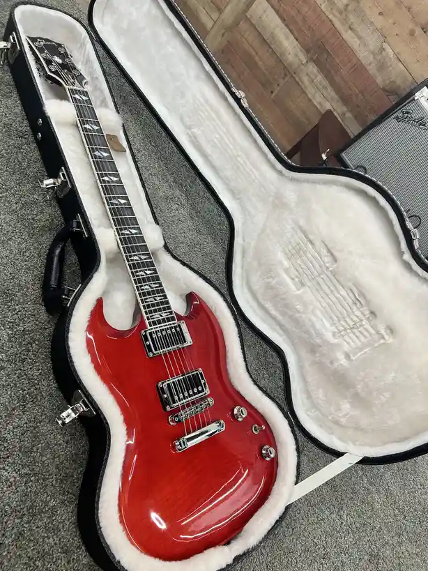 A glossy red electric guitar with a black fretboard and diamond inlays rests inside an open black hardshell case lined with…
