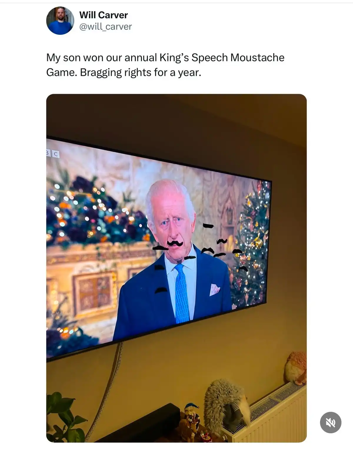 A television screen displays a photo of King Charles III, digitally edited with multiple cartoonish mustaches drawn over his…