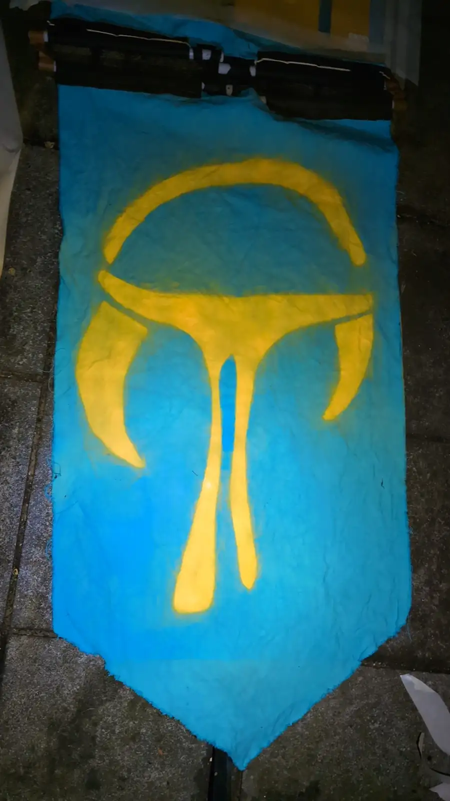 A handmade blue fabric banner with a yellow symbol resembling a stylized 'T' with curved arms and a circular top, laid on a…