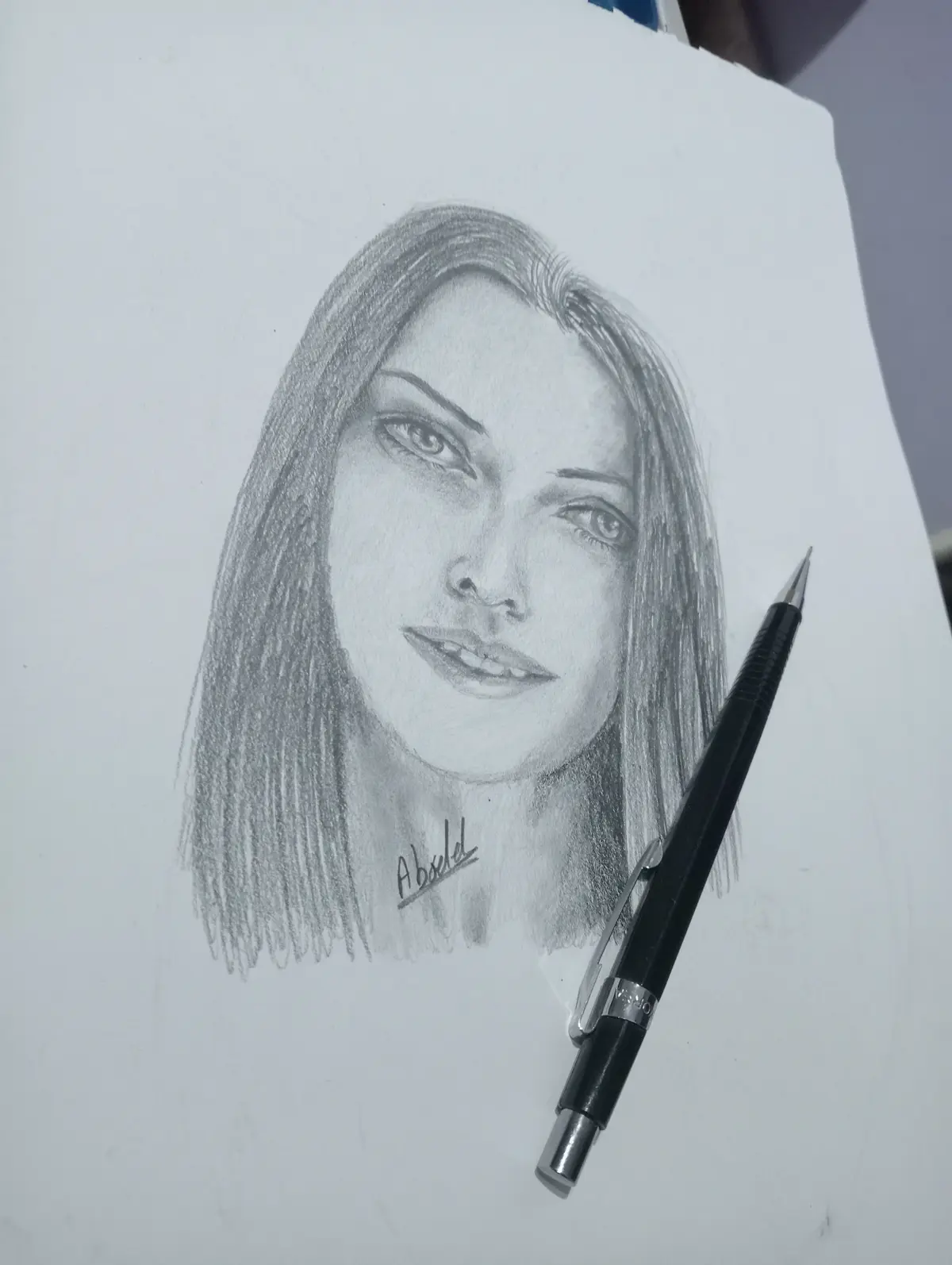 A detailed pencil sketch of a woman's face on white paper, signed 'Absel' near the neck, with a black mechanical pencil…