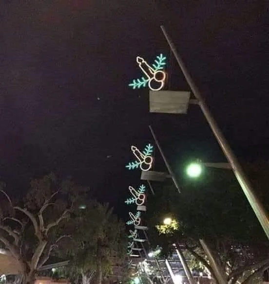A nighttime photo shows a row of streetlights decorated with glowing neon lights shaped like champagne flutes and…