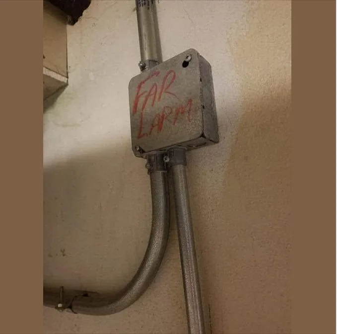 A close-up photo shows a metal electrical box mounted on a wall, connected to metal conduit pipes. The box has red…