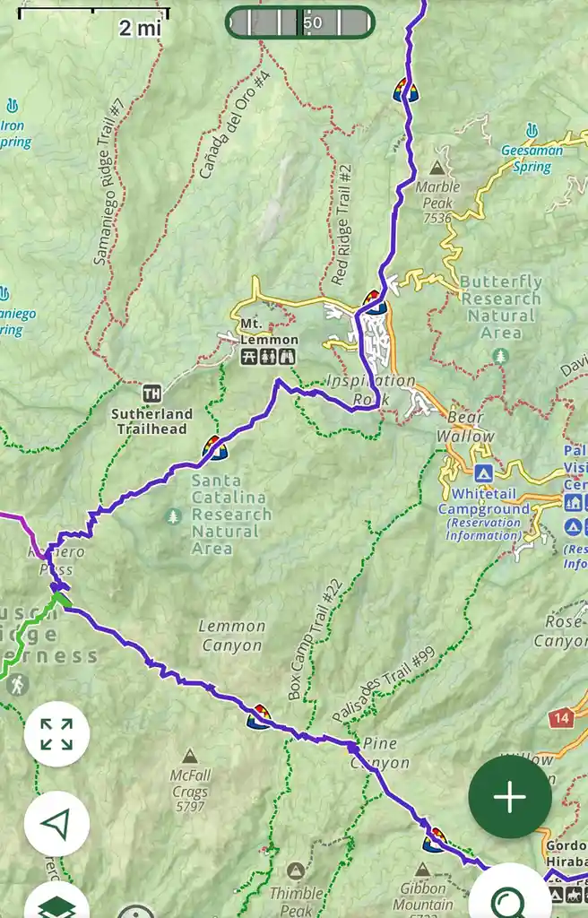 A hiking map app screenshot showing a purple trail winding through mountainous terrain with labeled peaks, trails, and…