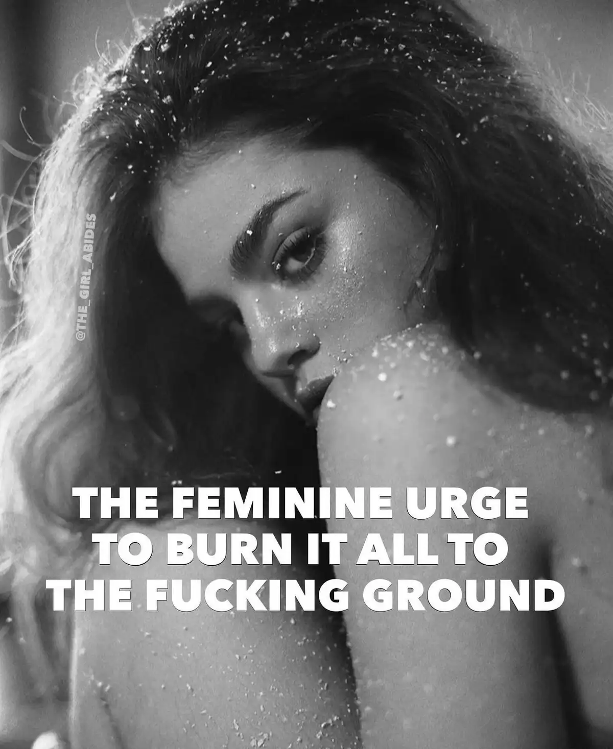 A black-and-white photo shows a woman with wet hair and skin, looking intensely at the camera through what appears to be a…
