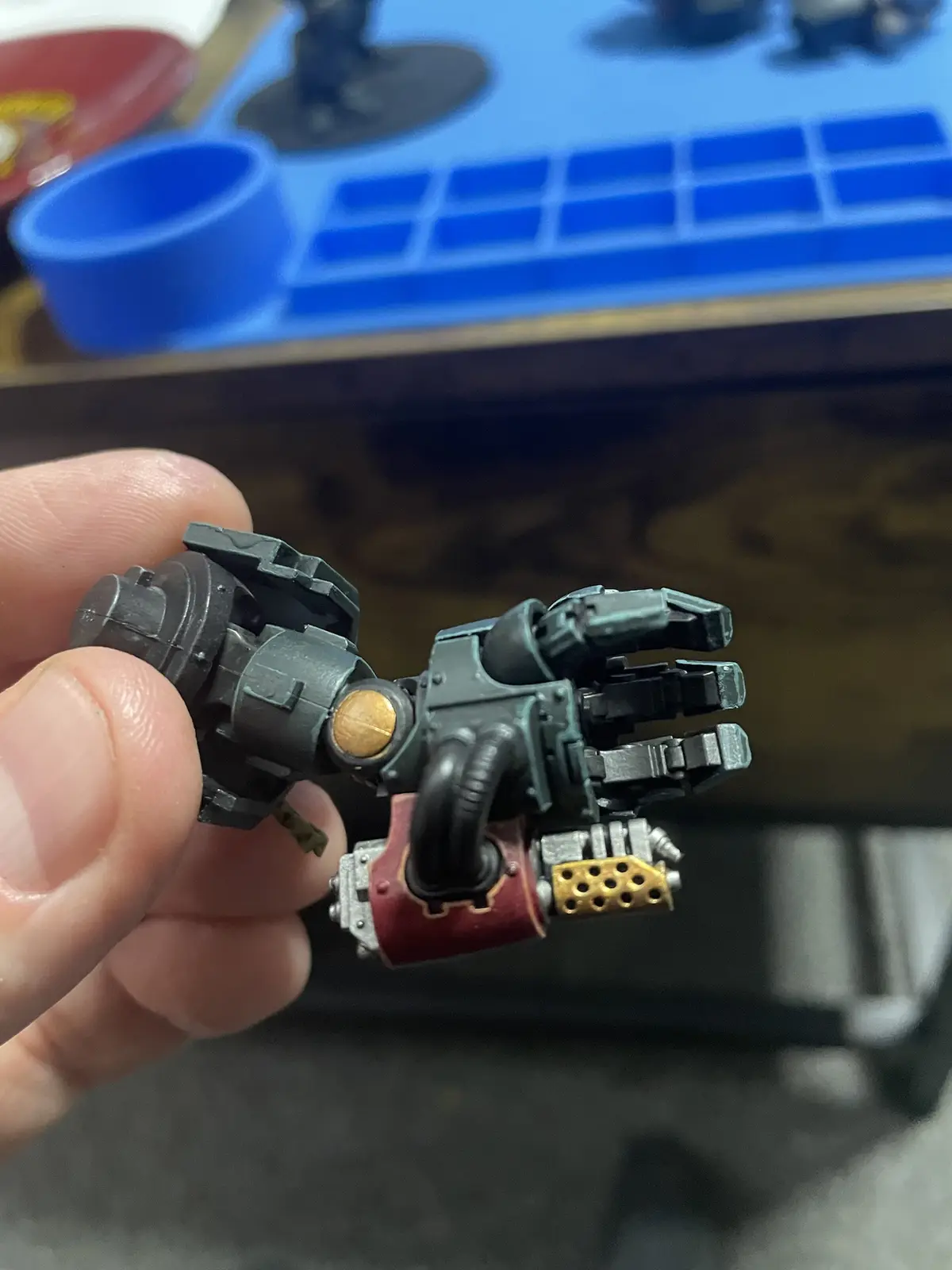 A close-up photo shows a person's fingers holding a detailed, painted miniature robotic hand with mechanical parts, pipes…