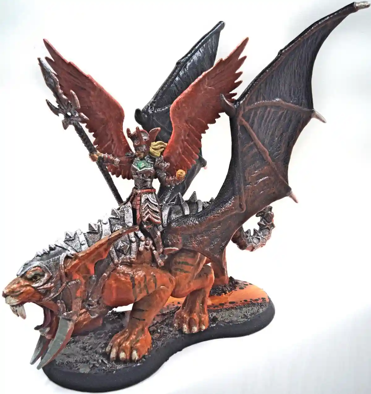 A painted miniature figurine shows a fantasy warrior with wings, mounted on a large, armored, winged beast resembling a…