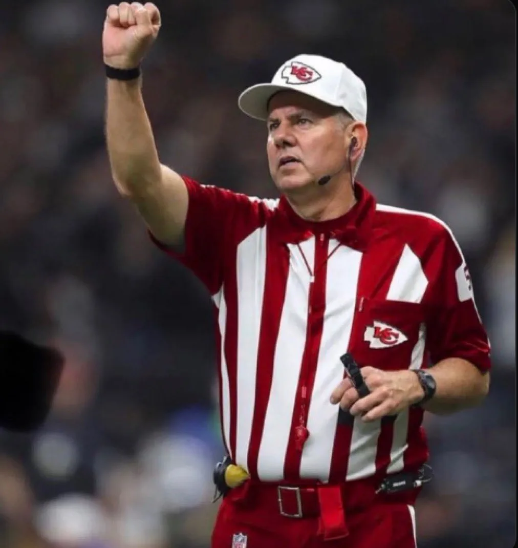 A close-up photo of an NFL referee wearing a red and white striped shirt and a white cap with the Kansas City Chiefs logo…