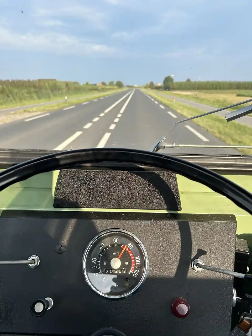 A first-person view from inside a vehicle, likely a vintage tractor or truck, showing a dashboard with a speedometer reading…