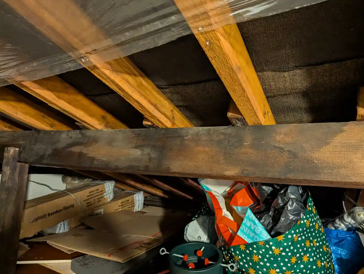 A cluttered attic space with exposed wooden beams and insulation, containing cardboard boxes labeled 'Completely Bamboo…