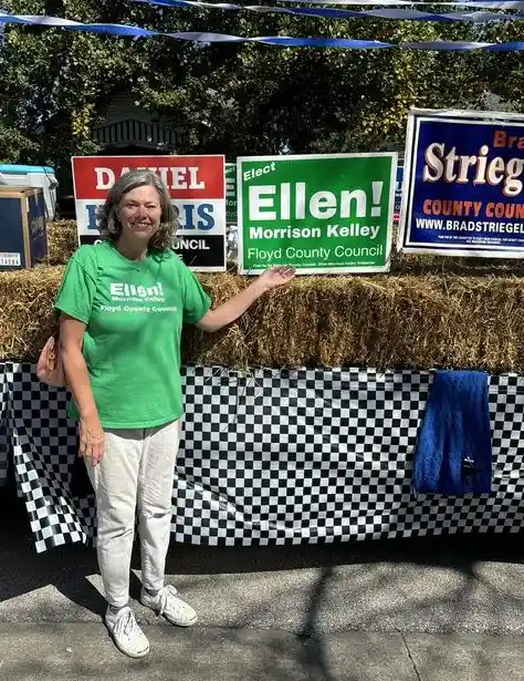 A smiling woman in a green t-shirt that reads 'Ellen! Morrison Kelley Floyd County Council' stands outdoors in front of hay…