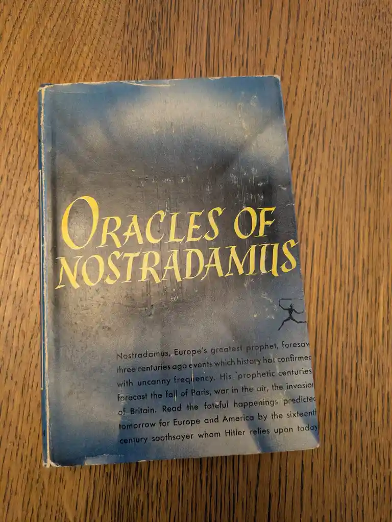 A worn, blue hardcover book titled 'Oracles of Nostradamus' rests on a wooden surface. The cover features gold lettering and…