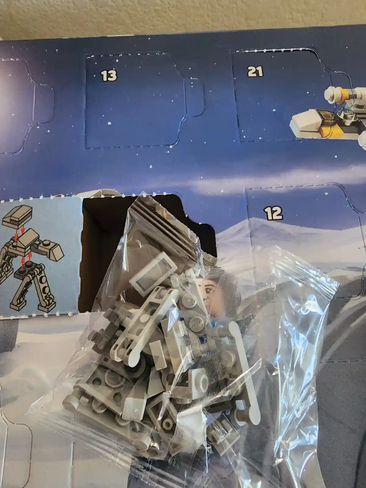 A close-up photo shows a ripped-open day 12 compartment of a Lego Star Wars Advent Calendar, with a clear plastic bag…