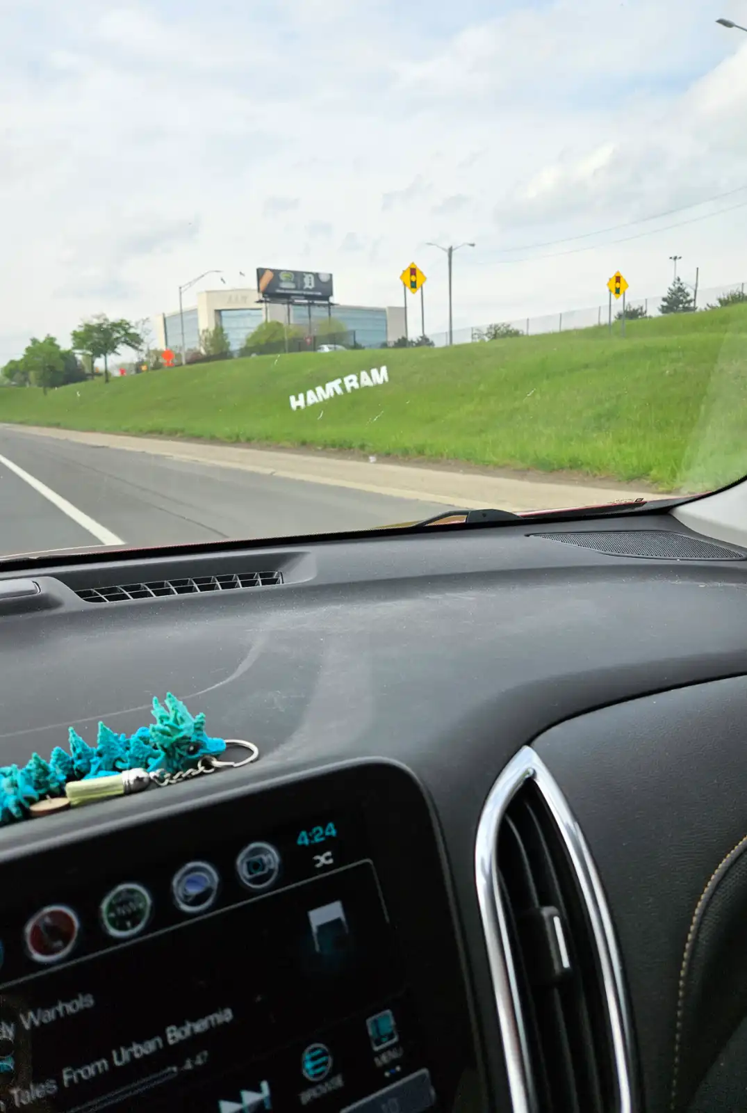 A photo taken from inside a car shows a grassy hillside with the word 'HAMTRAM' spelled out in white letters. The dashboard…