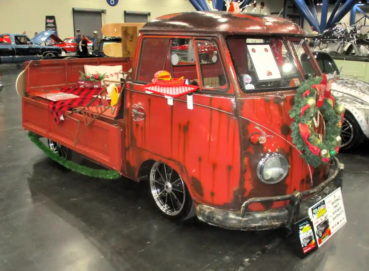 a red vintage volkswagen pickup truck is decorated for christmas with a wreath on the front, green garland along the bottom…