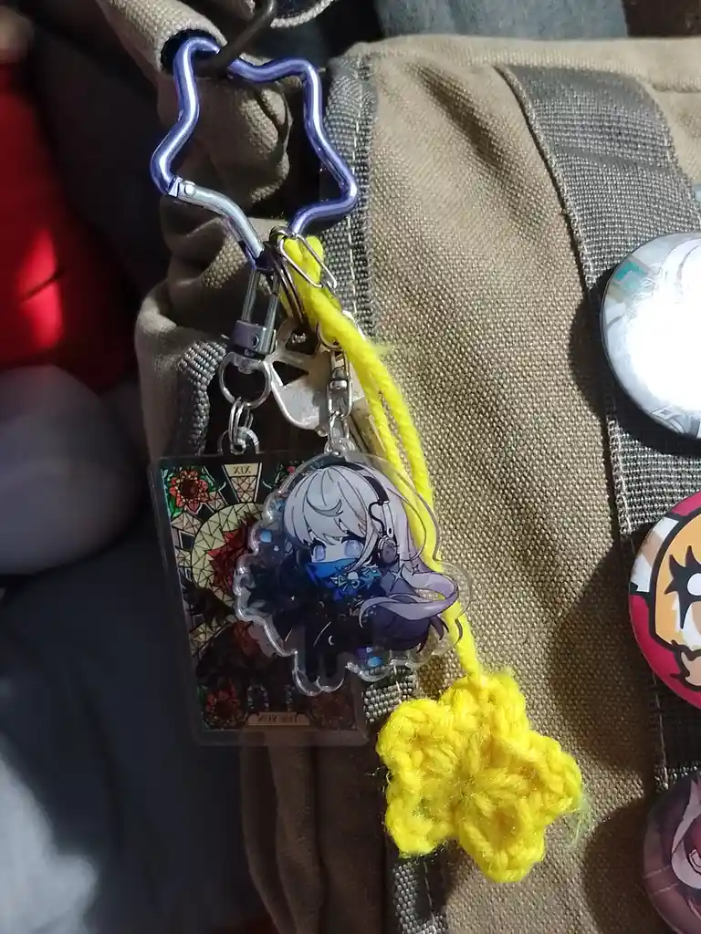 A close-up photo shows an anime-style keychain featuring a character with silver hair and headphones, attached to a tan…