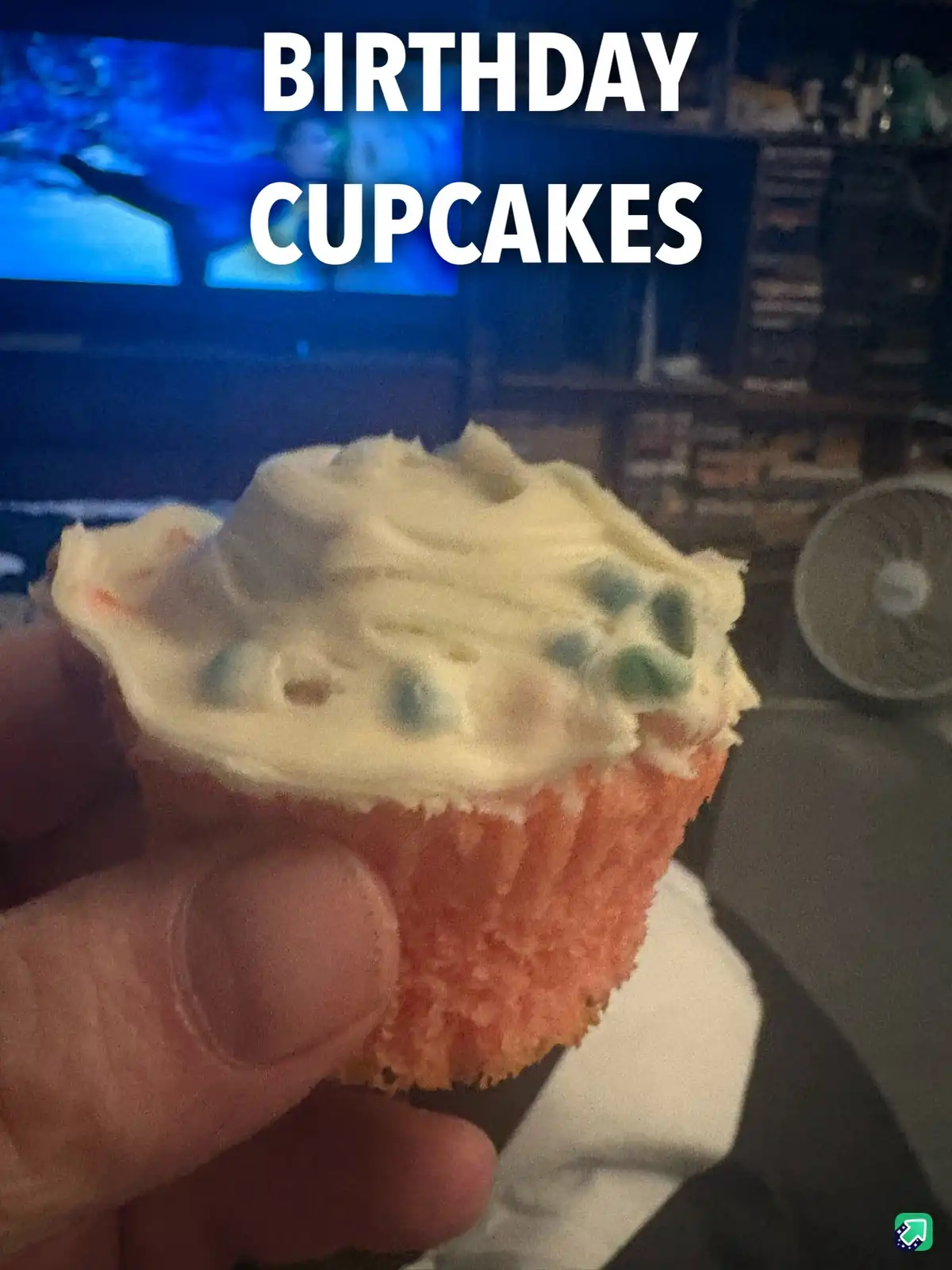 A hand holds a single, plain cupcake with white frosting and sparse blue sprinkles, labeled 'BIRTHDAY CUPCAKES' in bold…