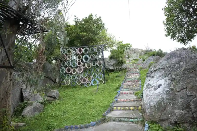 An outdoor staircase and wall decorated with colorful painted tires, surrounded by green grass and large rocks under an…