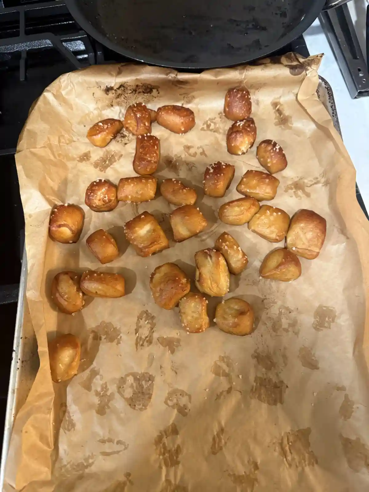 A baking sheet lined with parchment paper holds golden-brown, salted pretzel bites arranged in a rough spiral pattern. A…