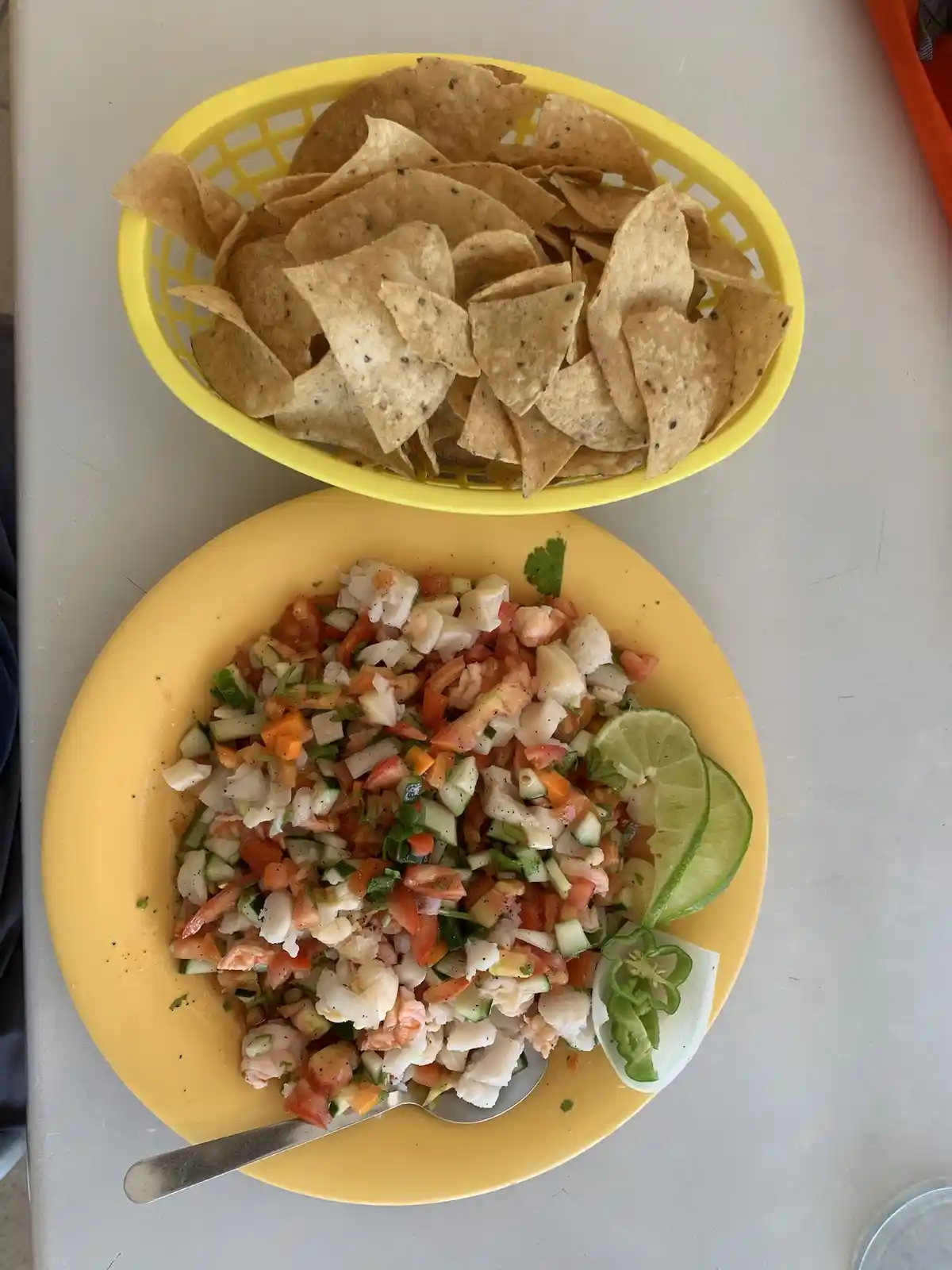 An overhead photo shows a yellow plate with ceviche (shrimp, fish, tomato, cucumber, lime, jalapeño) and a yellow basket of…