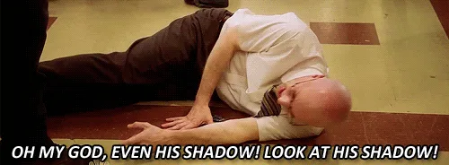 A man in a white shirt and dark pants lies on a tiled floor, initially looking at his own shadow with exaggerated shock. In…