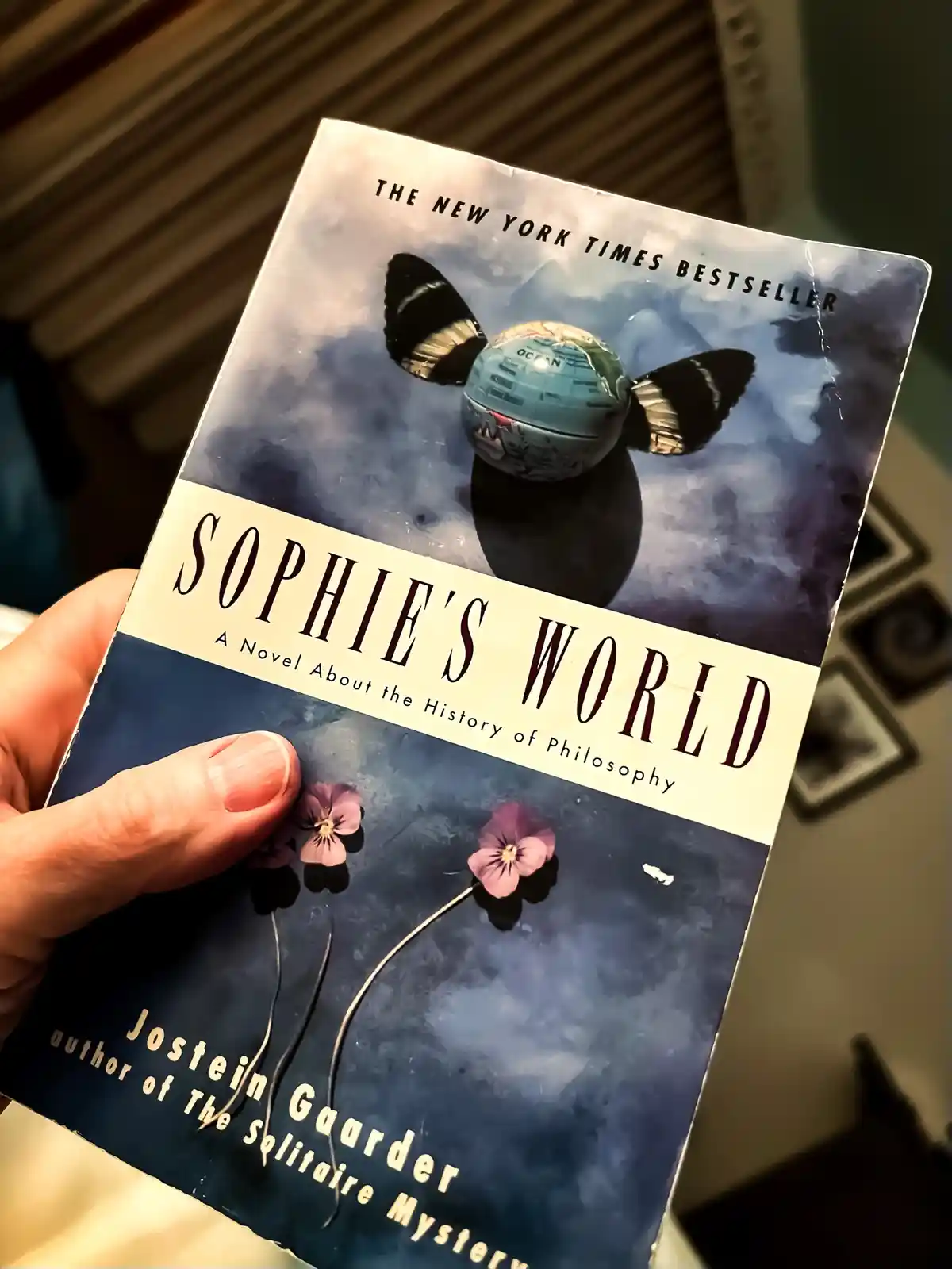 A hand holds a well-worn copy of Jostein Gaarder's 'Sophie's World,' a novel about the history of philosophy, featuring a…