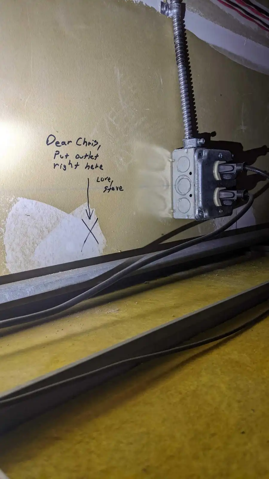 A close-up photo shows a wall with handwritten text that reads 'Dear Chris, Put outlet right here' with an arrow pointing to…