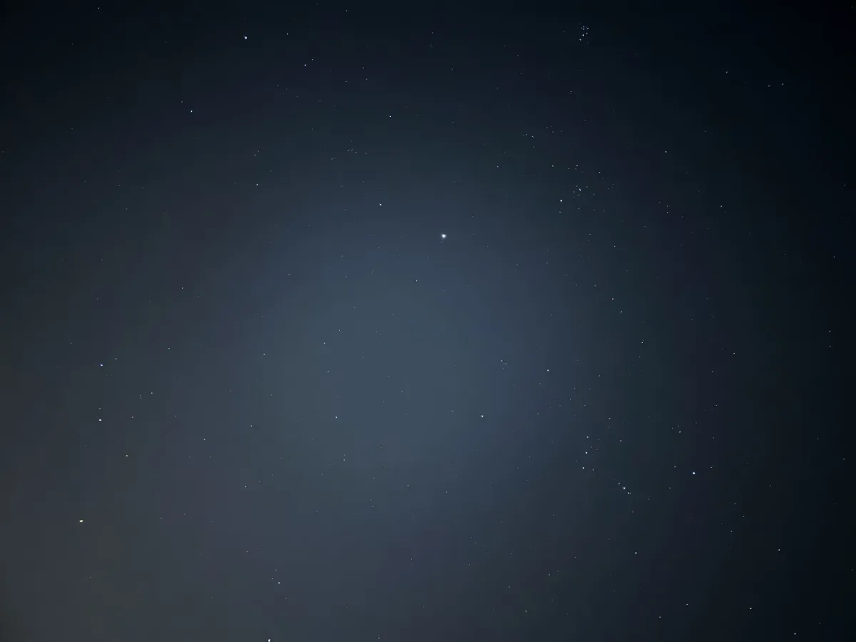 A dark night sky filled with numerous small, scattered stars, with a slightly brighter star near the center. The image has…