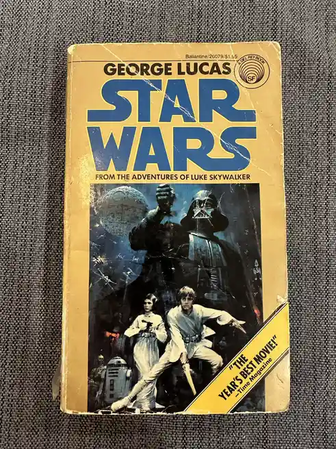 A well-worn, yellow-covered paperback book titled 'Star Wars: From the Adventures of Luke Skywalker' by George Lucas…
