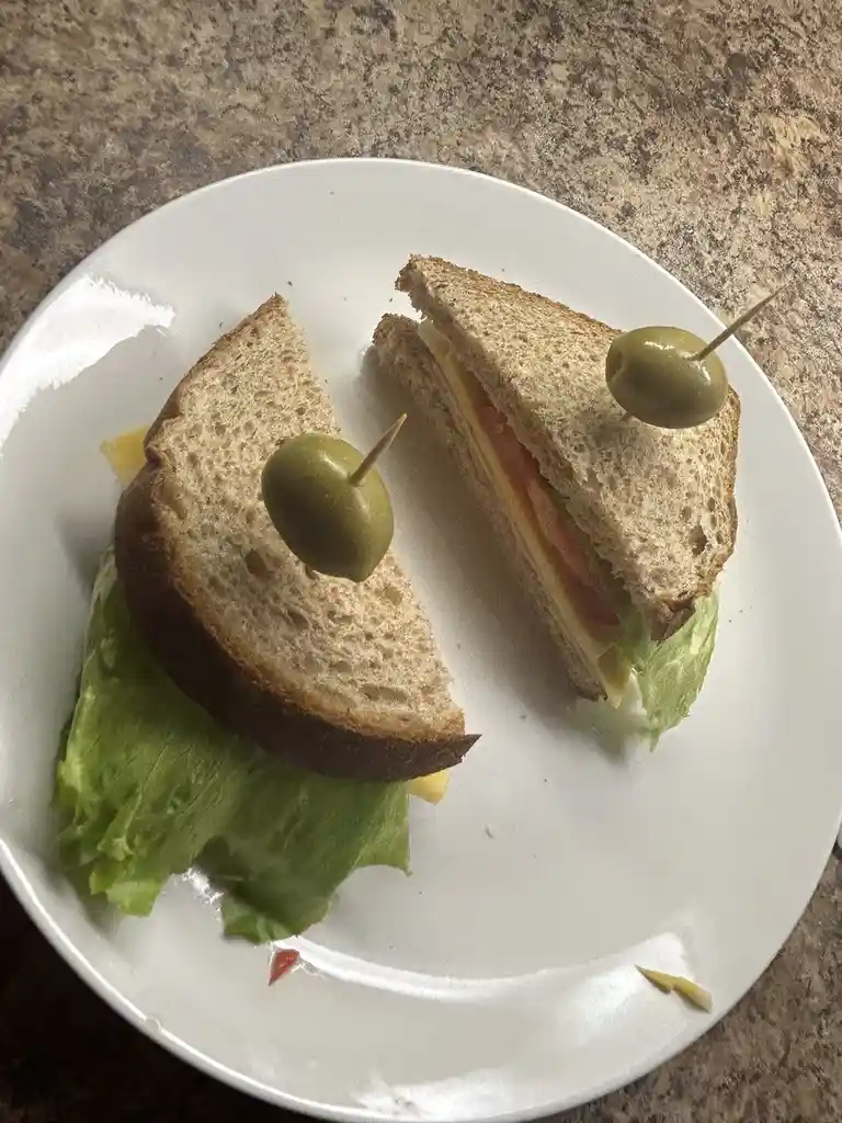 A plate holds two triangular sandwich halves made with whole wheat bread, lettuce, tomato, and cheese, each secured with a…