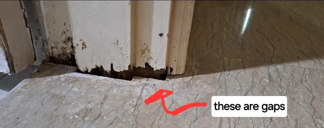 A close-up photo shows the bottom of a worn, peeling white door frame with visible gaps between the frame and the…