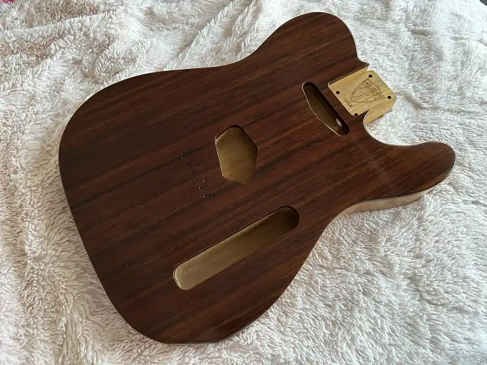 A polished, dark wood guitar body with cutouts for pickups and hardware, resting on a fluffy white blanket. The text overlay…