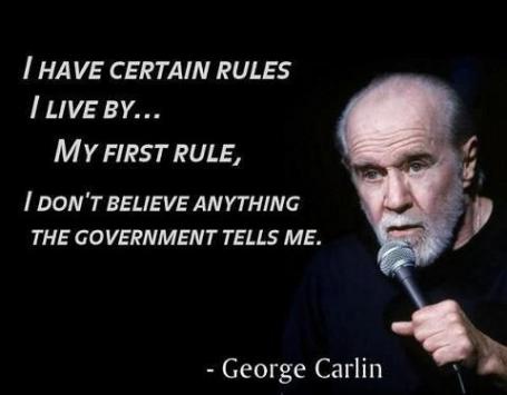A black background image features comedian George Carlin holding a microphone, looking directly at the viewer with a serious…