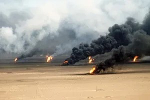 a wide shot of a desert landscape with multiple oil wells on fire, emitting thick black smoke into the sky. the ground is…