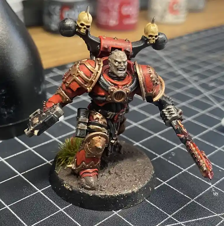 A heavily painted miniature of a grim, armored warrior with skulls on his weapon, standing on a base with green grass…