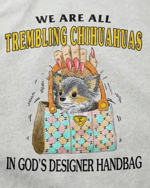 A gray t-shirt graphic shows a small chihuahua peeking out of a colorful, patterned designer handbag with a hand holding the…