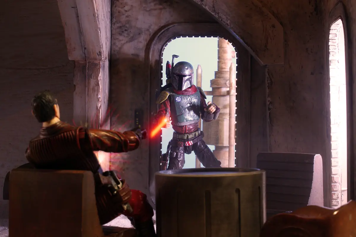 A Star Wars action figure of Boba Fett stands in an arched doorway, aiming a blaster at another figure seated in a chair…