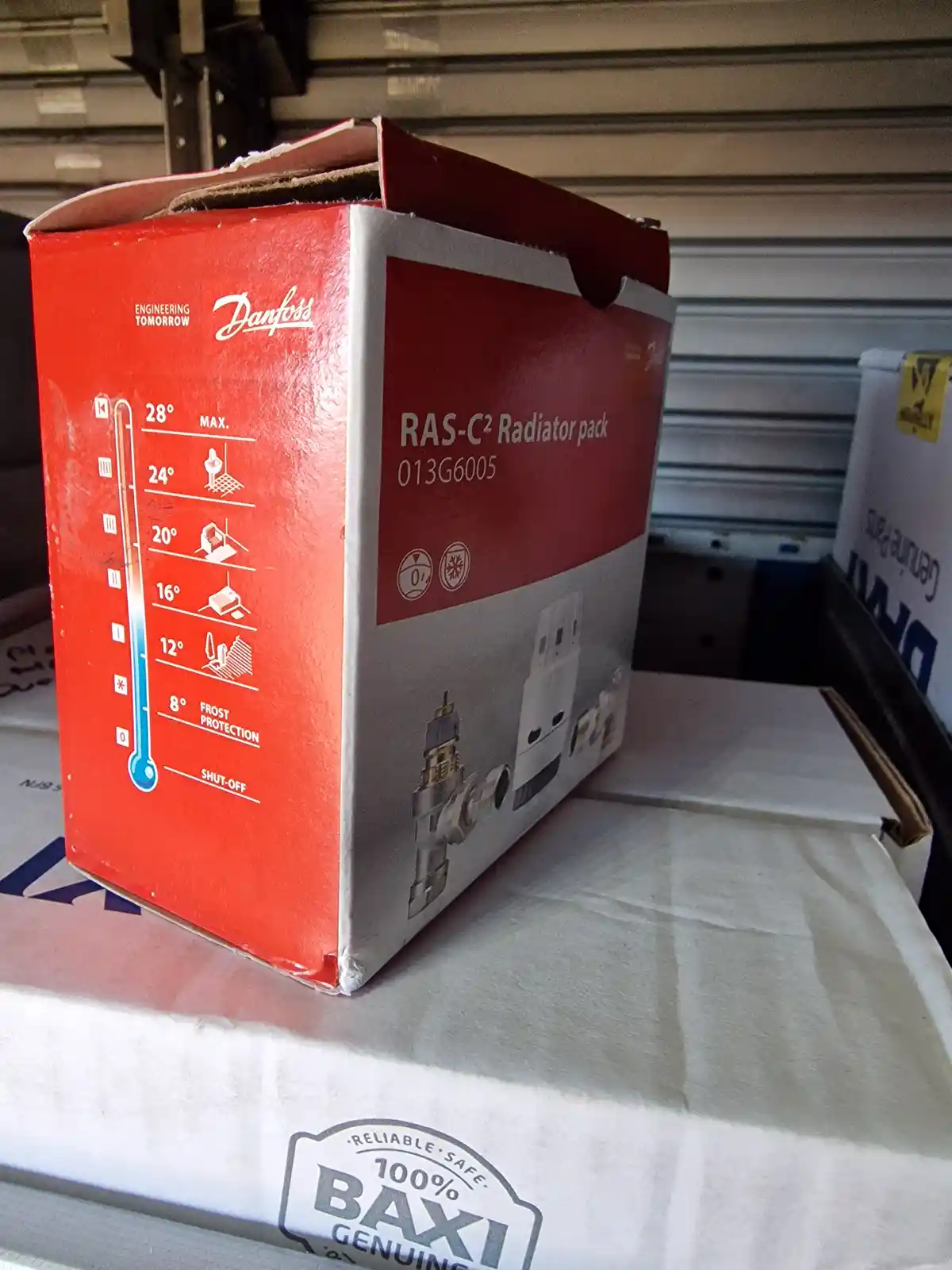 A red Danfoss radiator pack box shows a thermometer graphic with temperature settings from 0 to 28 degrees Celsius…