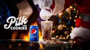 A person in a Santa Claus costume pours milk from a glass into a tall glass containing crushed cookies, next to a can of…