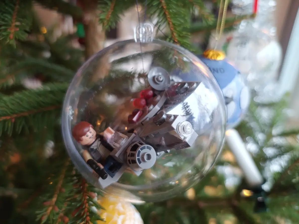 A close-up photo shows a clear Christmas ornament hanging on a tree, containing a Lego Star Wars scene with a minifigure and…
