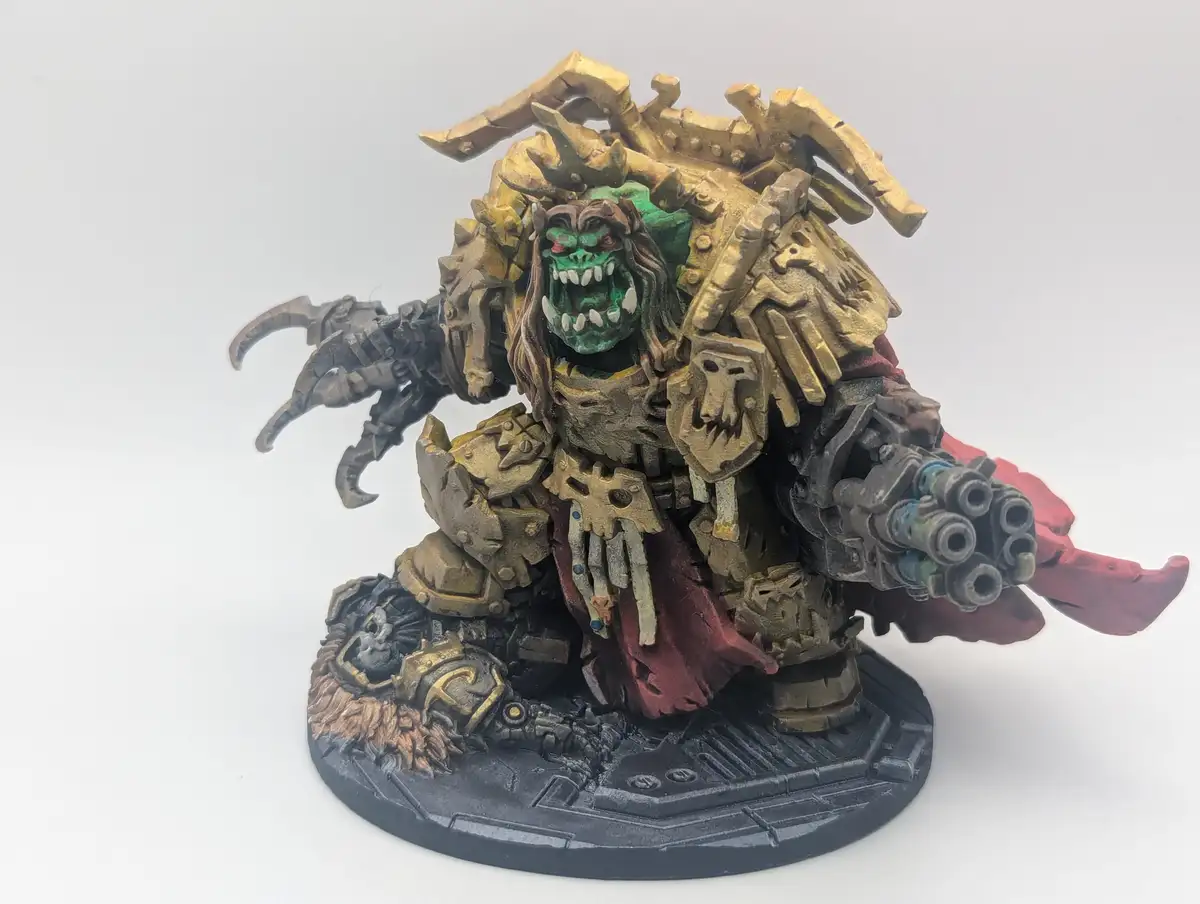 A heavily detailed, painted miniature of a green-skinned, monstrous warlord with gold armor, a red cape, and a…