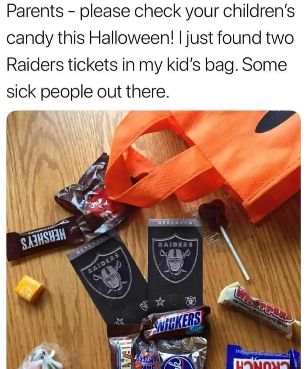 An orange Halloween trick-or-treat bag sits on a wooden floor next to various candies including Hershey's, Snickers…