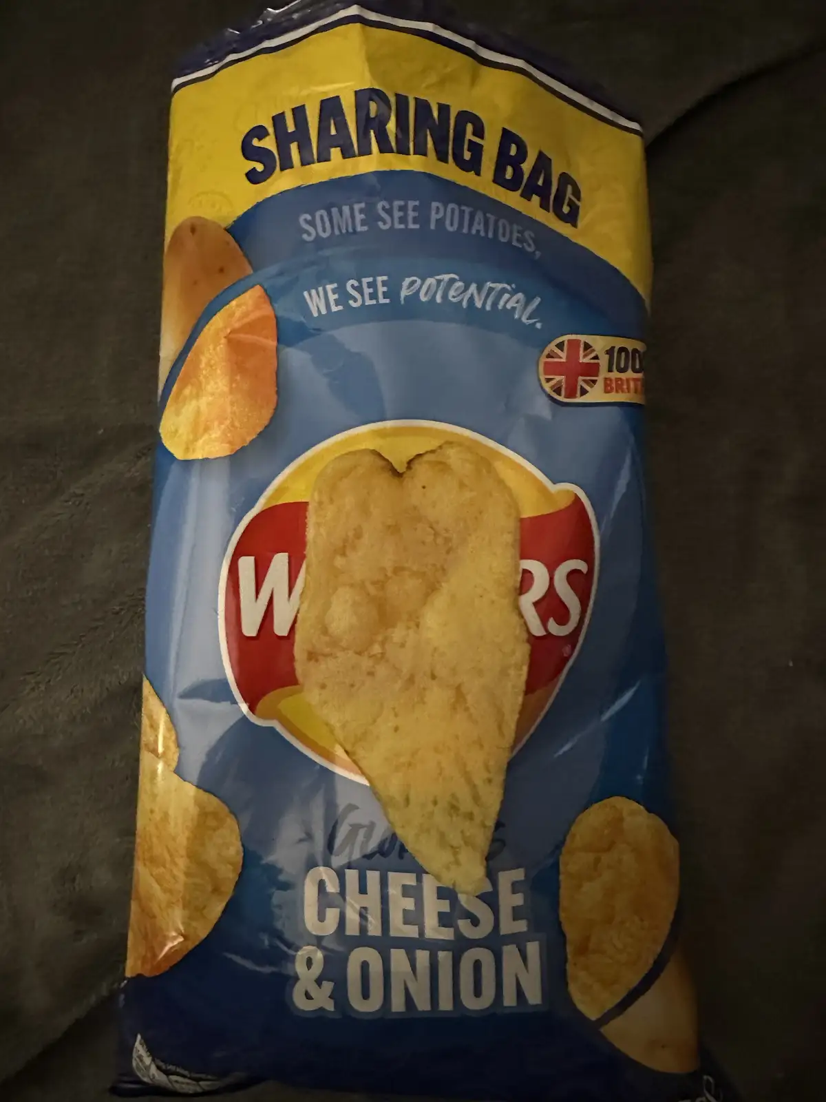 A close-up photo of a Wotsits Cheese & Onion sharing bag of crisps, featuring the brand's slogan 'some see potatoes, we see…