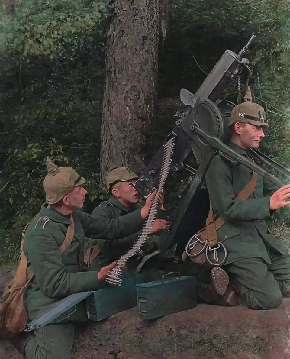 Three soldiers in green uniforms and distinctive spiked helmets are operating a large machine gun in a forest setting. One…