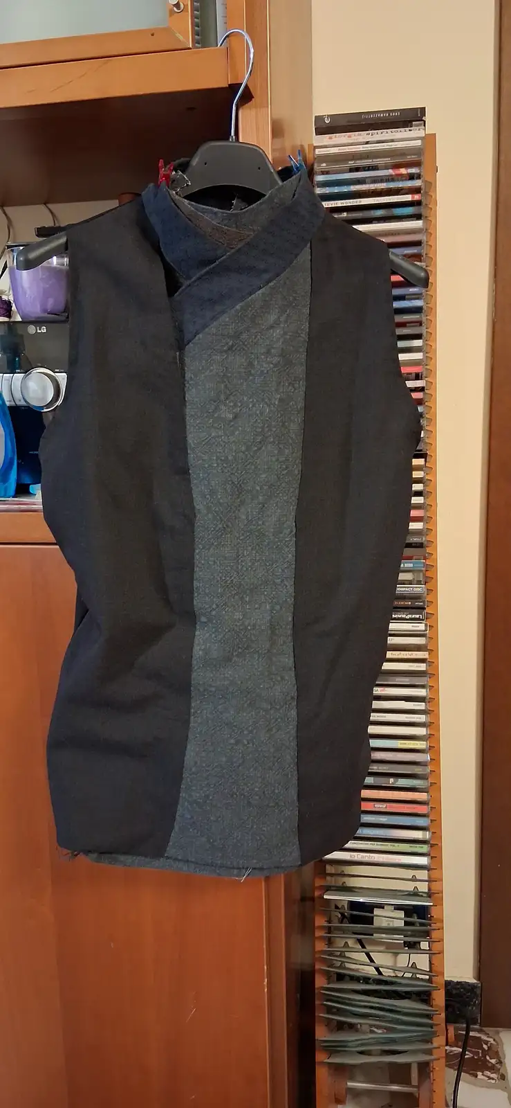 A handmade sleeveless vest with a dark grey and black color-blocked design hangs on a black hanger, secured with red…