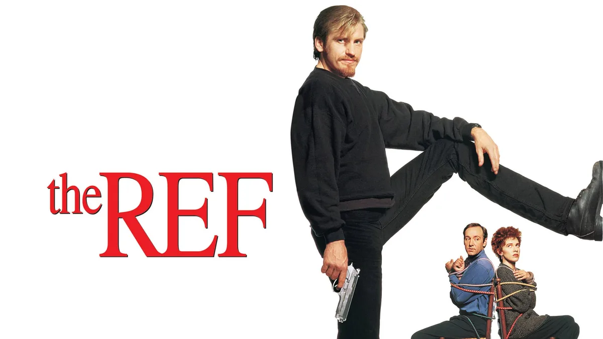 A promotional poster for the 1994 film 'The Ref' shows a man in a black sweatshirt and pants holding a gun while kicking his…